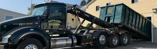 Green dump truck with a dumpster in front of a building.