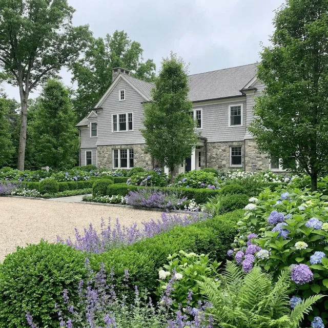 Stately home with a well-manicured garden featuring purple and white flowers.