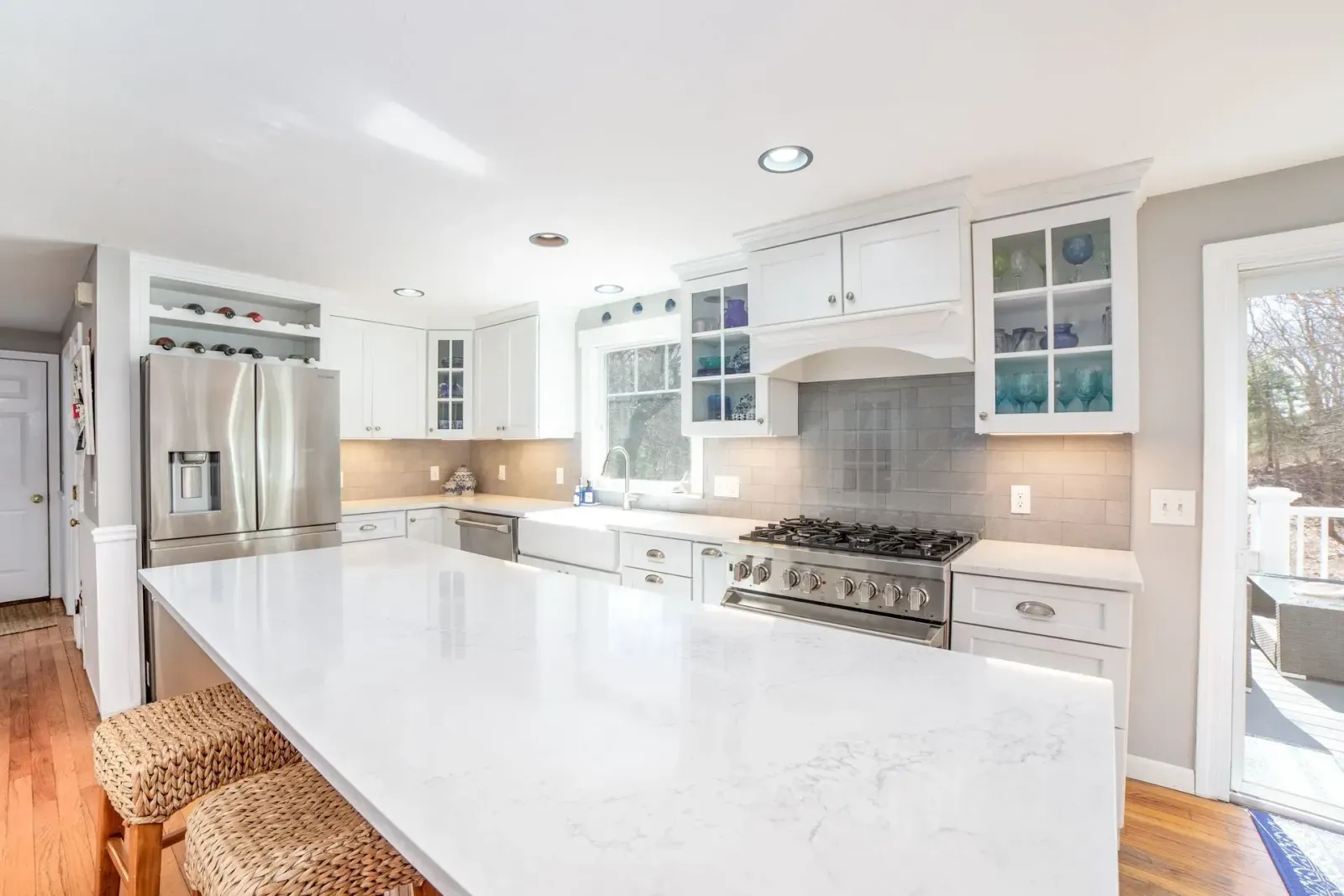 Bright white kitchen with marble island, stainless steel appliances, and large windows
