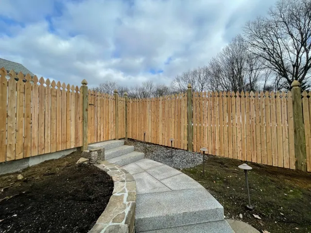 A wooden fence surrounds a stone walkway in a backyard.