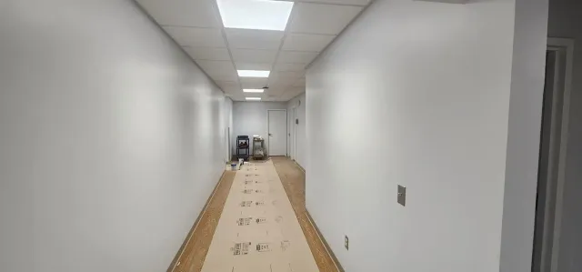 A long hallway with white walls and wooden floors is being painted.