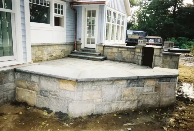 Raised bluestone terrace on a cut stone retaining wall with an outdoor kitchen