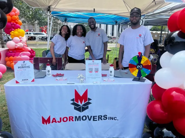 The Major Movers team at a community event behind a branded Major Movers table