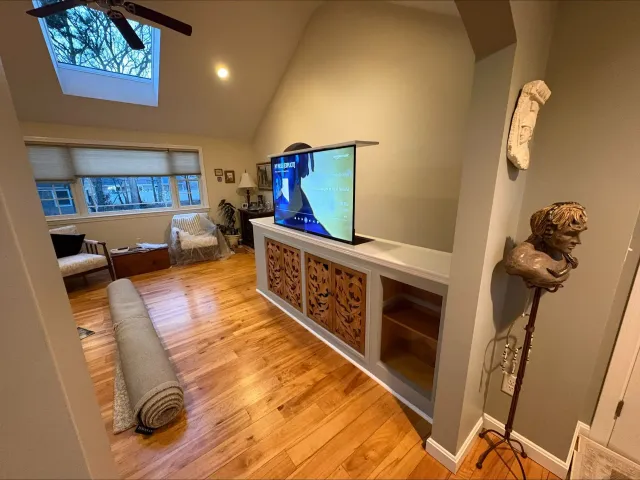 Living room with hardwood floors, sofa, wall-mounted TV, skylight, and decorative lion sculpture