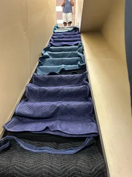 Staircase covered in blue moving blankets. Person standing at the top.