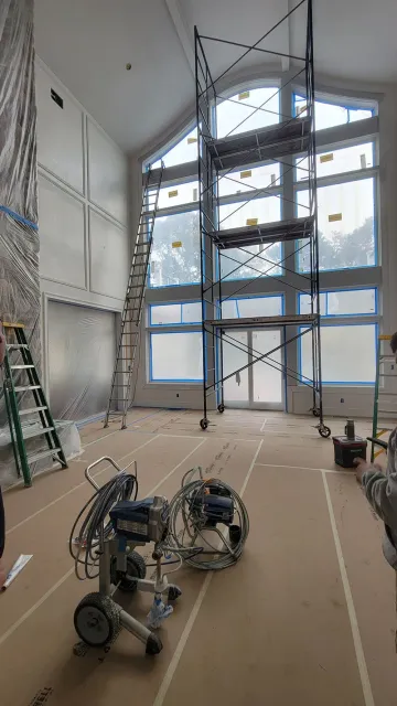 Scaffolded interior with tall blue-framed windows, ladders, and construction equipment on the floor