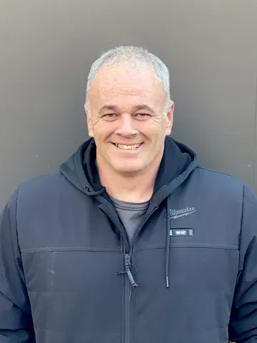 A professional headshot of a carpenter in a black Milwaukee jacket