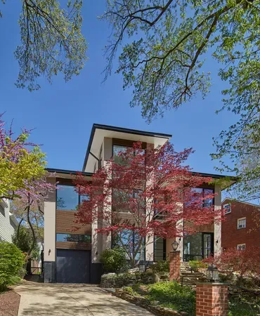 Modern two-story house with brick accents, red-leaf trees, and a blue sky viewed from the front yard