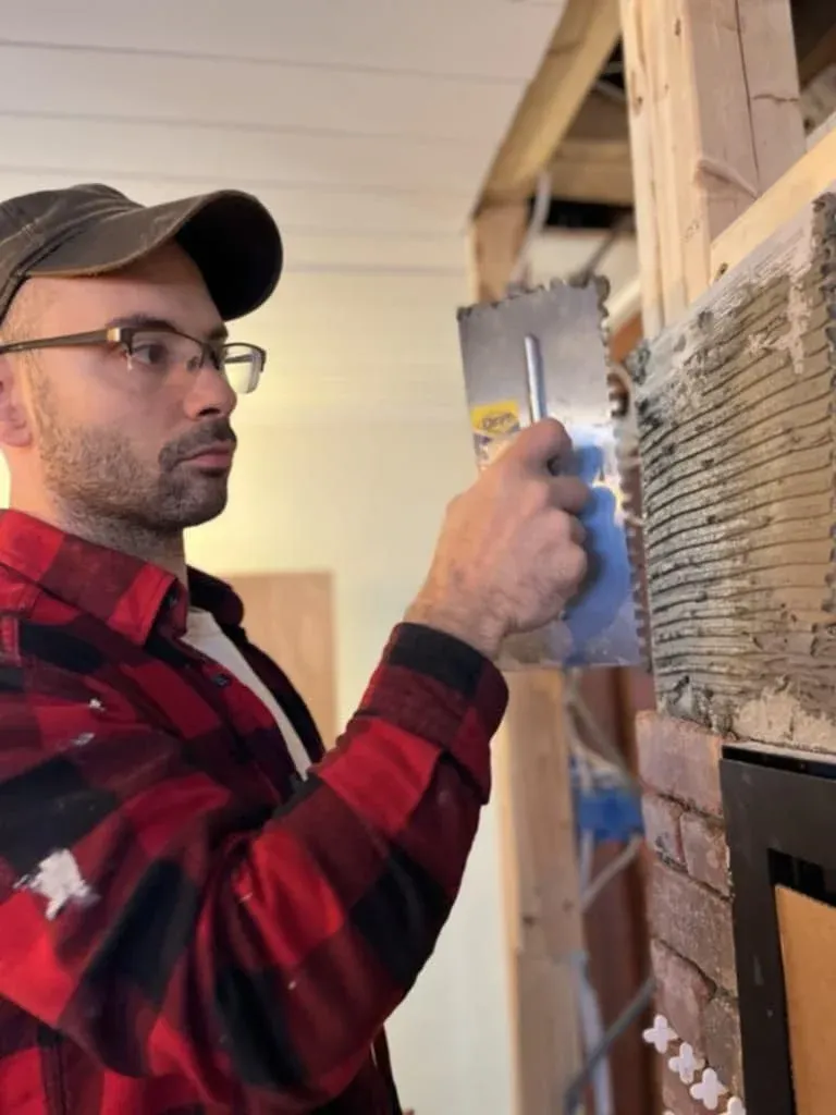Person in plaid shirt applying mortar on a wall with a trowel.