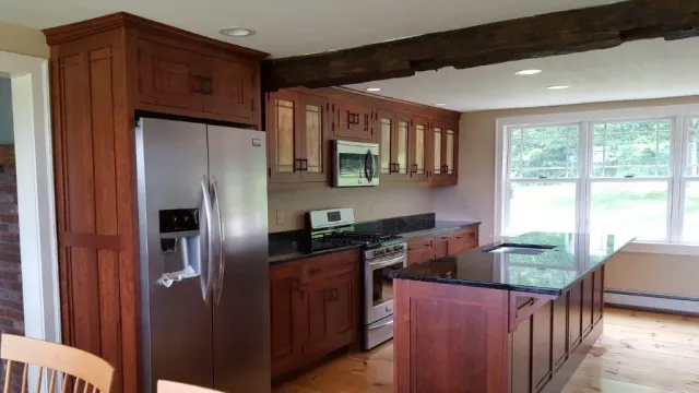 Modern kitchen with stainless fridge, dark wood cabinets, black island, and large windows overlooking a yard