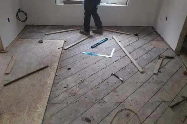 worker preparing a diagonal wood subfloor with leveling tools and measuring squares during a hardwood flooring replacement project