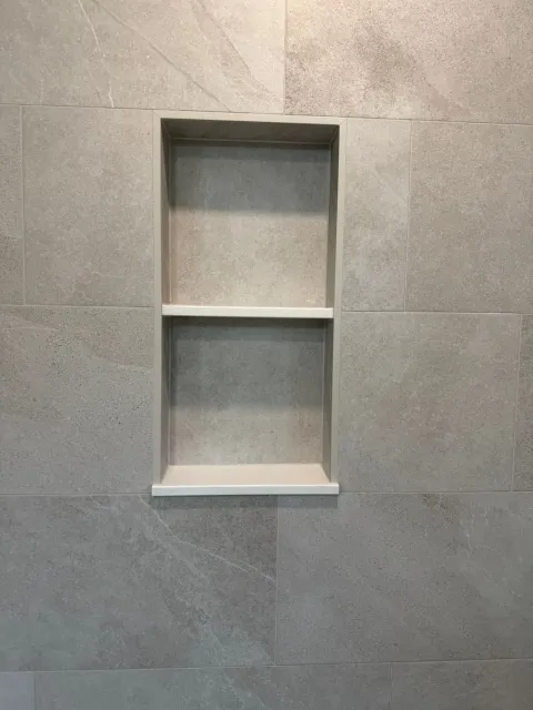 Two-shelf shower niche set flush into large-format stone-look porcelain, aligned to the tile joints