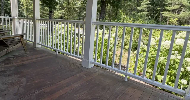 White vinyl railings installed along a covered porch overlooking a wooded backyard