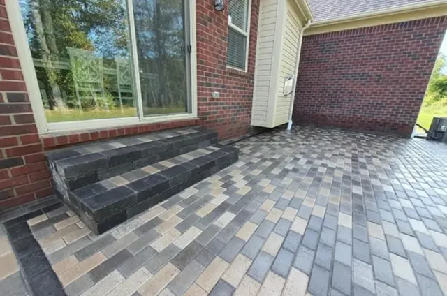 Brick house patio with gray pavers, steps, and large window beside a garage door