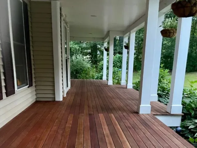 Stained wooden porch with white pillars and lush greenery, showcasing quality craftsmanship by Handymasters Painting Co. in Durham, NH.
