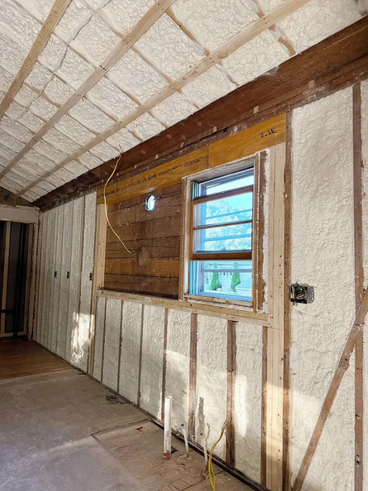 Interior view of a room with spray foam insulation on walls and ceiling, framing a window.