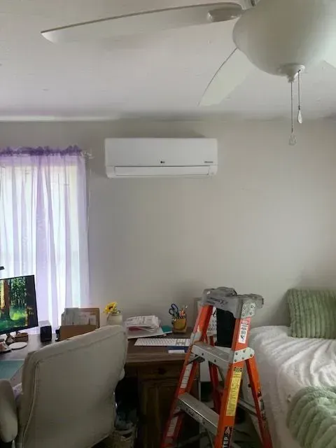 Living room with wall-mounted air conditioner, white sofa, desk, ceiling fan, and a ladder by the couch