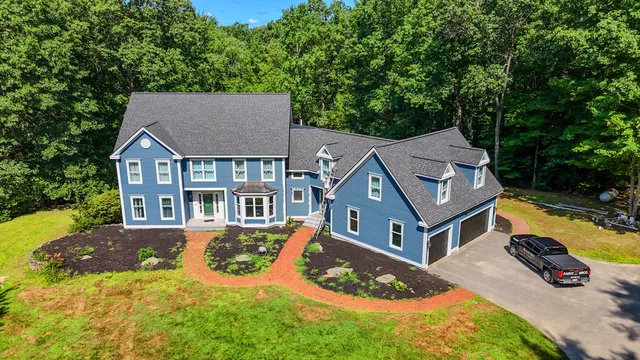 Aerial view of a large blue colonial home with dark shingle roof, brick driveway, and wooded backdrop in New England — exterior painted by Paint Pros MA.