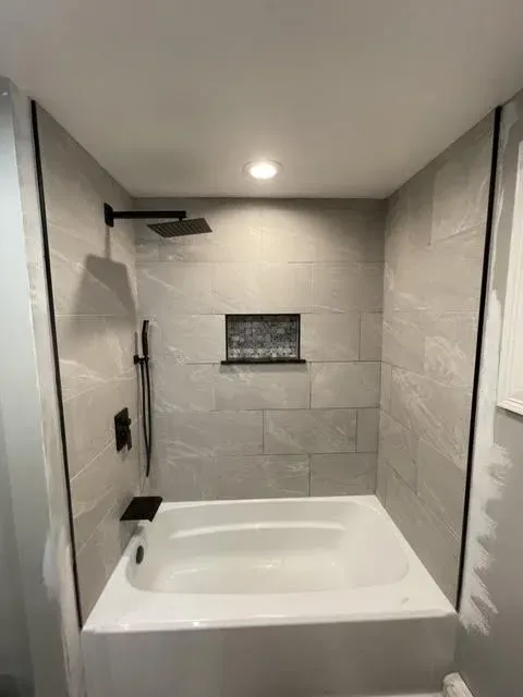 Modern walk-in shower with gray marble tiles, black fixtures, and a built-in niche for toiletries.