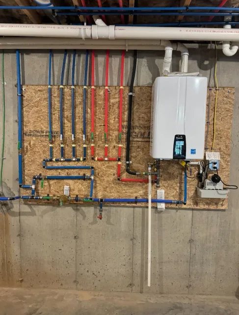 A water heater is mounted to a wall next to a bunch of pipes.