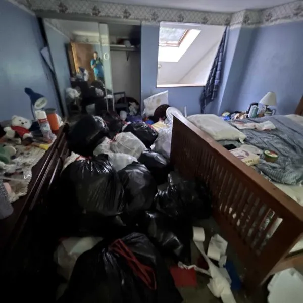 Before photo of a cluttered bedroom filled with trash bags and debris, part of a Delta Cleaning rental property cleanout in Plaistow NH