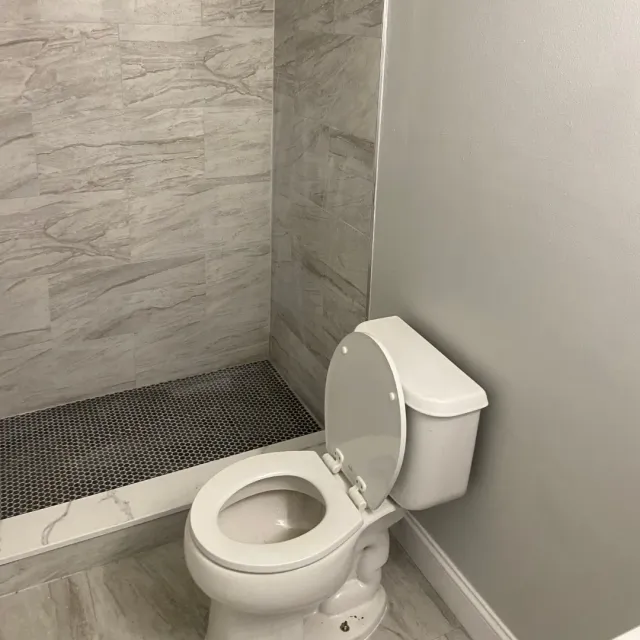 Tiled shower stall with wood-look gray porcelain and black penny-round floor by SF Construction in Hudson, MA