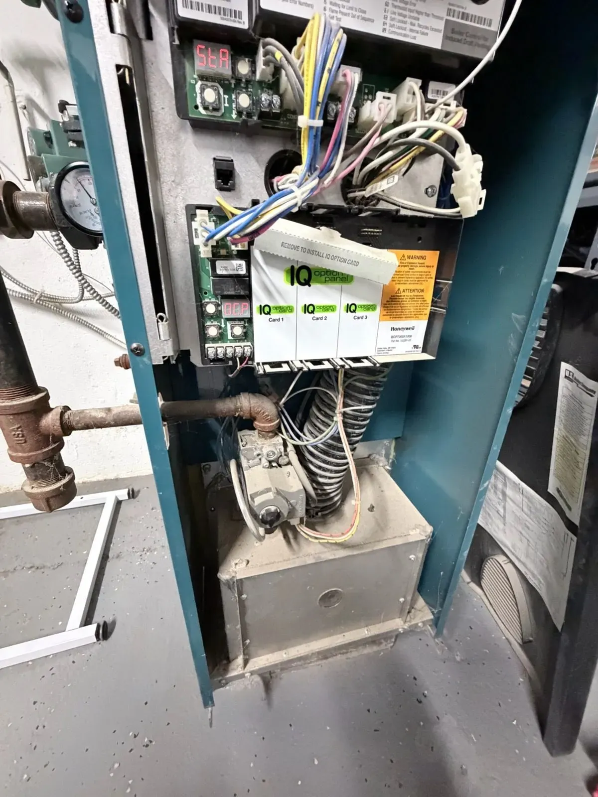 Electrical panel with exposed wiring and a white-green device mounted inside a metal cabinet.