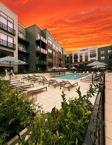 Apartment complex with a pool and lounge chairs under a fiery sunset