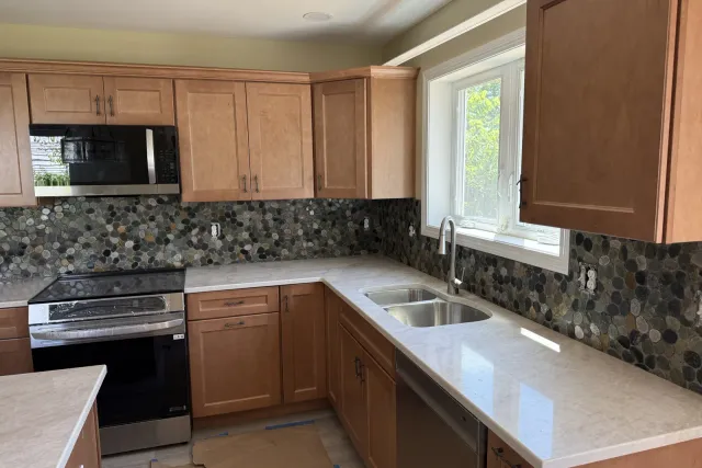 Kitchen backsplash of pebble-stone mosaic behind the range with maple cabinets and quartz counters — kitchen backsplash installation by Dmtilellc in Plainville, CT