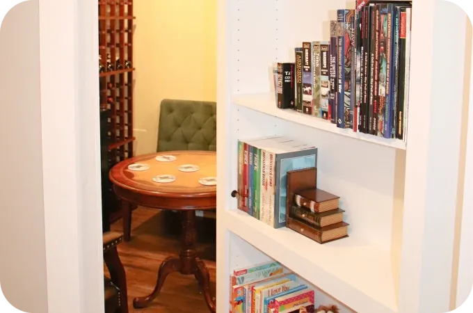 White built-in bookshelf with books and boxes; round wooden table with coasters nearby.