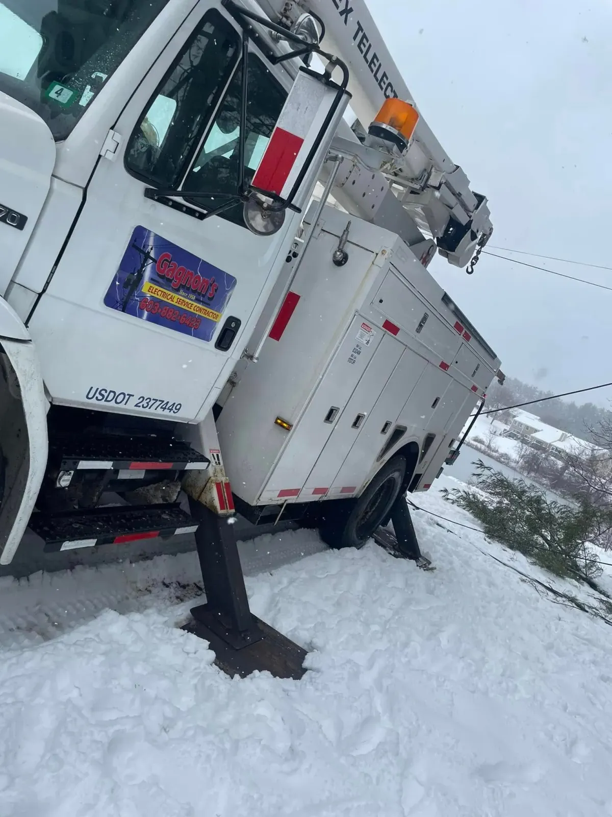 White utility truck stuck in deep snow on a snowy roadside, with mountains in the background