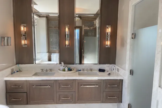 A bathroom with a double sink vanity, mirrors, and sconces. Features a glass shower door to the right.