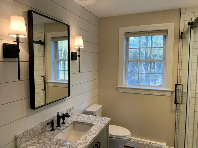 Bathroom with white shiplap walls, a window, vanity, mirror, and toilet.