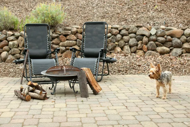 A laid paver patio with seating and a fire bowl, backed by a fieldstone wall