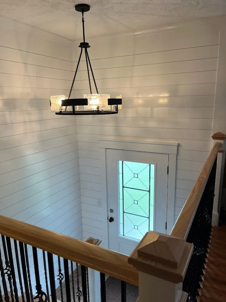 a modern, black chandeleir installed in the entry way of a home casting intrersting shadows around the ship lapped entryway walls