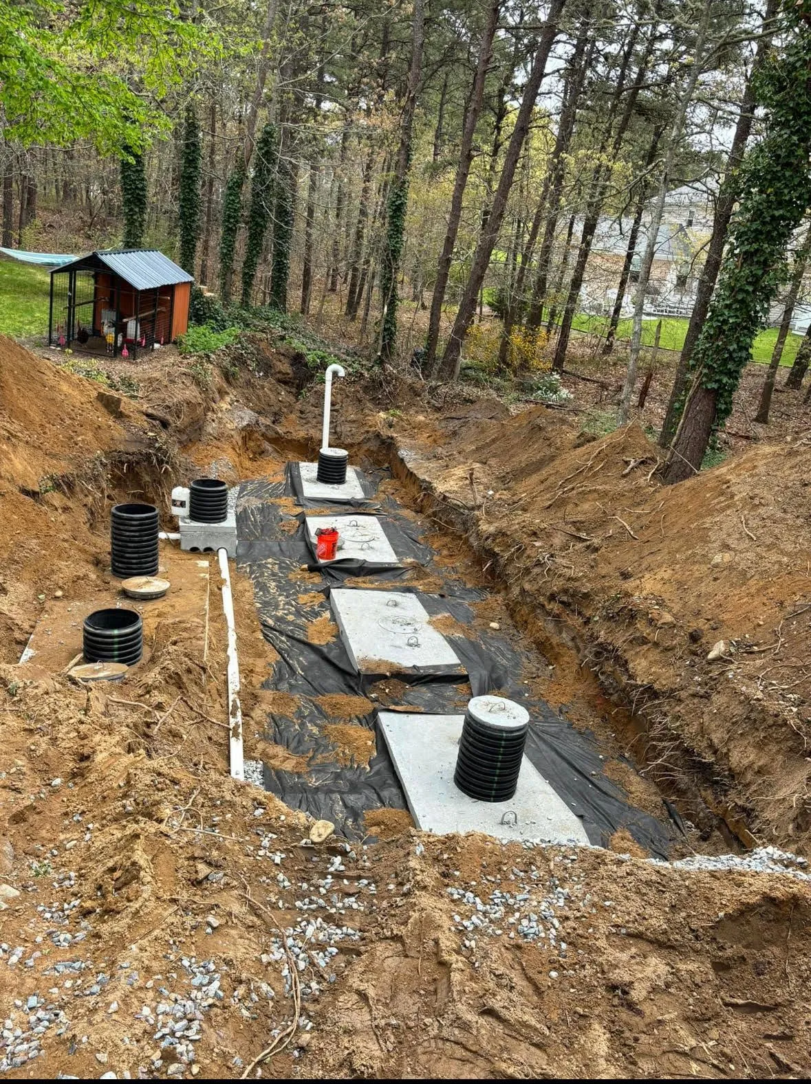Excavated area for a septic system installation. Gray tanks and white pipes are in a trench of dirt.