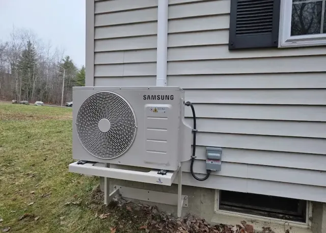 Samsung outdoor heat pump unit mounted on a beige house wall with a grassy lawn nearby.