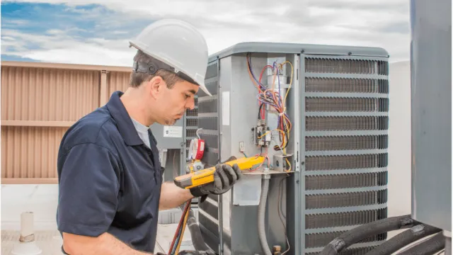 A man wearing a hard hat and gloves is working on an air conditioner.