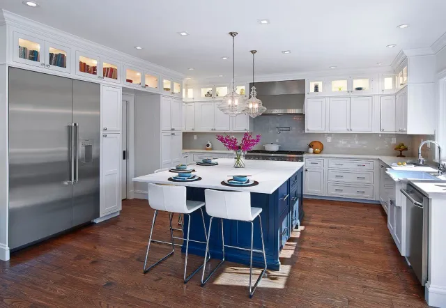 Bright modern kitchen with white cabinets, stainless fridge, island seating, and blue chairs on a wood floor