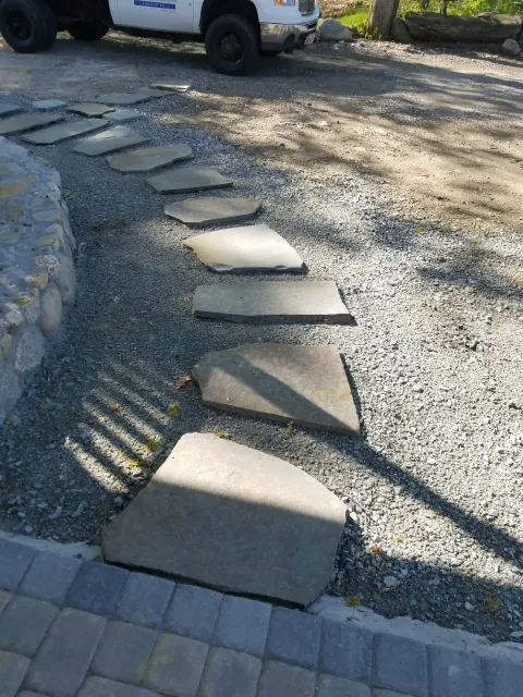 Stepping stones across a gravel path beside a curved stone border and parked vehicle