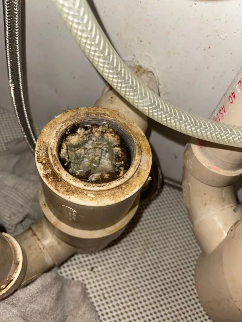 Dirty sink drain with debris buildup and connected pipes.