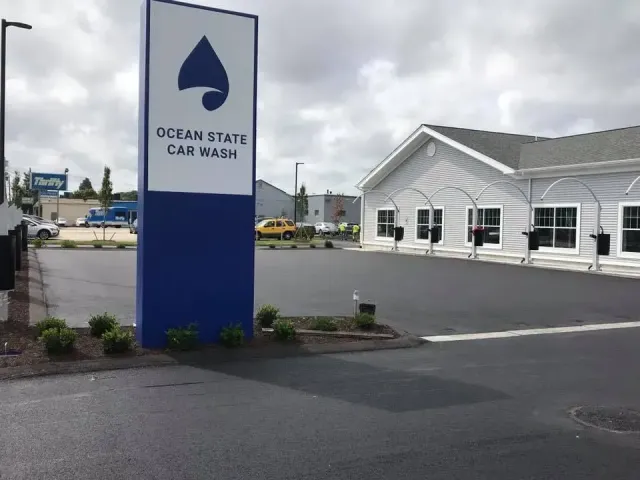 Sign for Ocean State Car Wash with building in the background on a cloudy day.