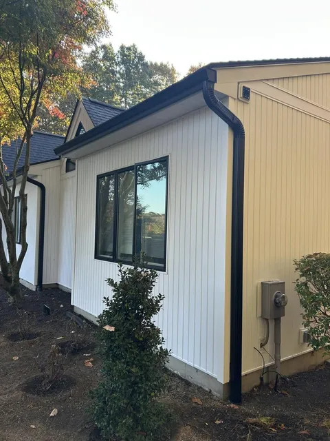 Black seamless gutter and downspout installed along white board-and-batten siding