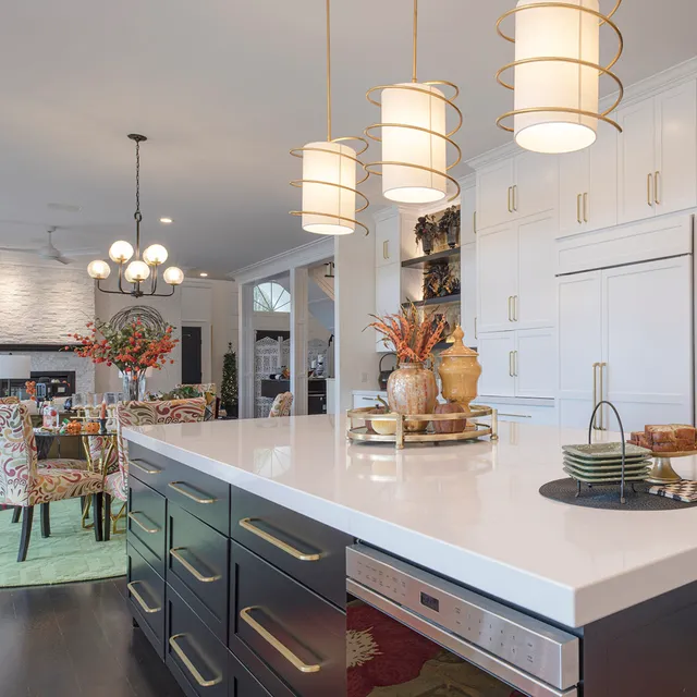 Modern kitchen with white cabinets, black island, and white countertop. Gold pendant lights and decorative items add elegance.