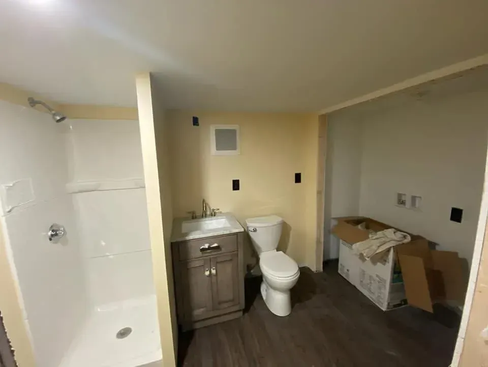Unfinished bathroom with shower, vanity, toilet, and boxes on the floor.