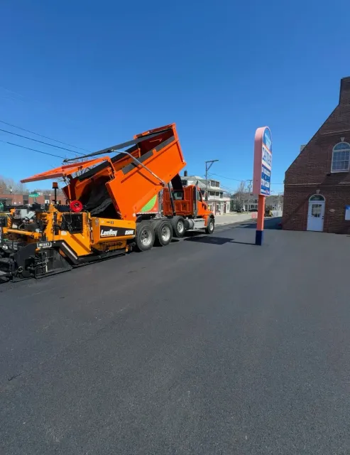 Orange snowplow truck on a sunny street beside a brick building and blue sky