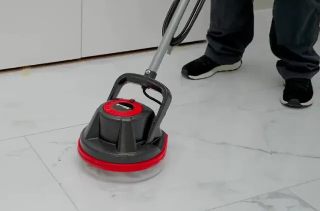 A person using a red and black floor polisher on a white tiled floor.