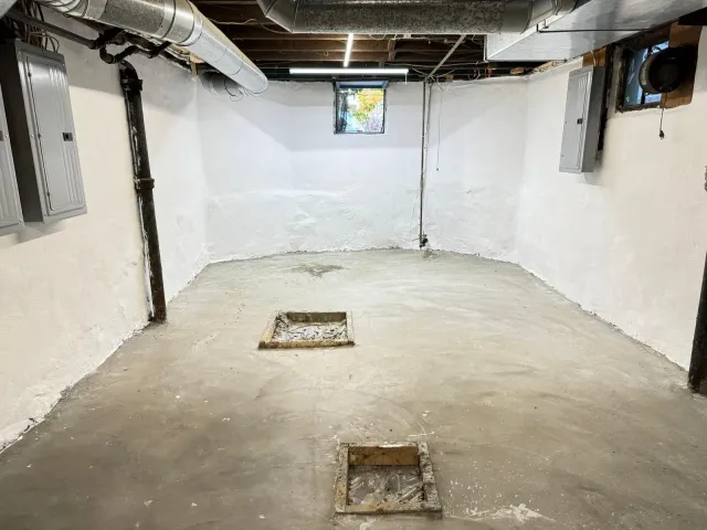 Empty, white-painted basement room with concrete floor, electrical boxes, and ductwork.
