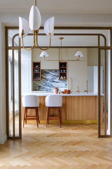 Modern kitchen with a brass-framed archway, herringbone floor, and marble backsplash