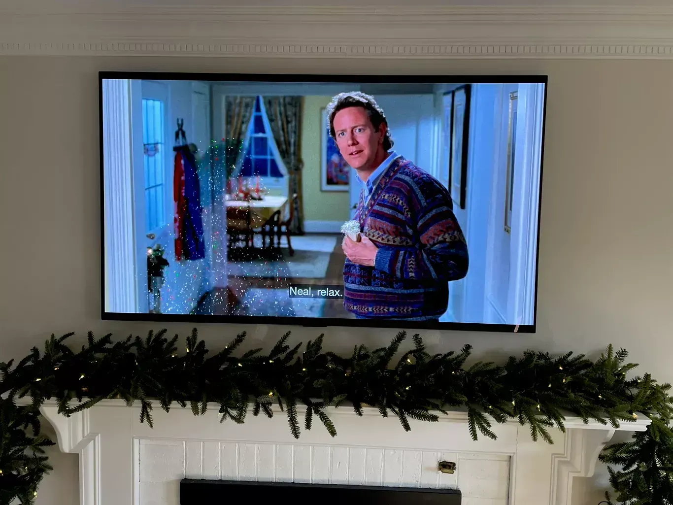 Man in a striped sweater holding a mug in a living room, shown on a wall-mounted TV.
